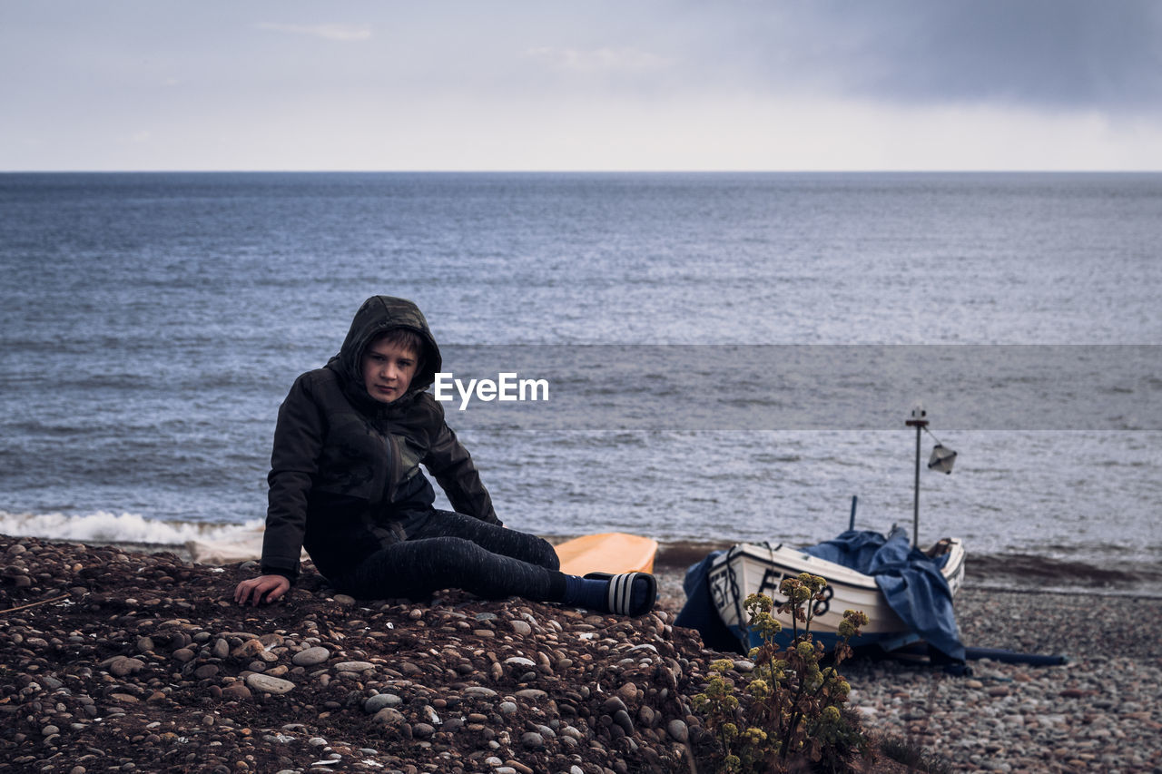 side view of man sitting on rock at beach against sky