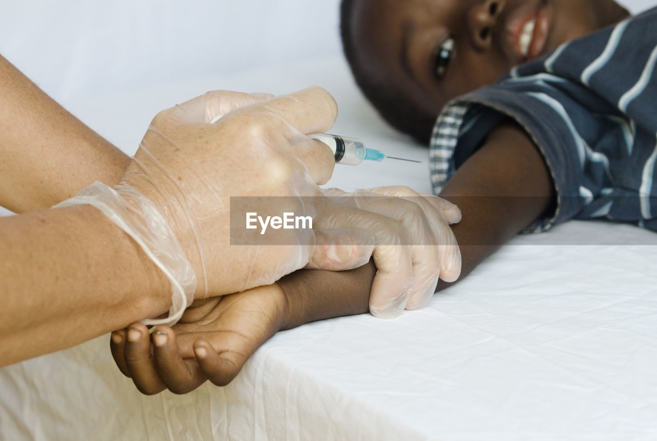 Cropped hands of doctor injecting patient on bed in hospital