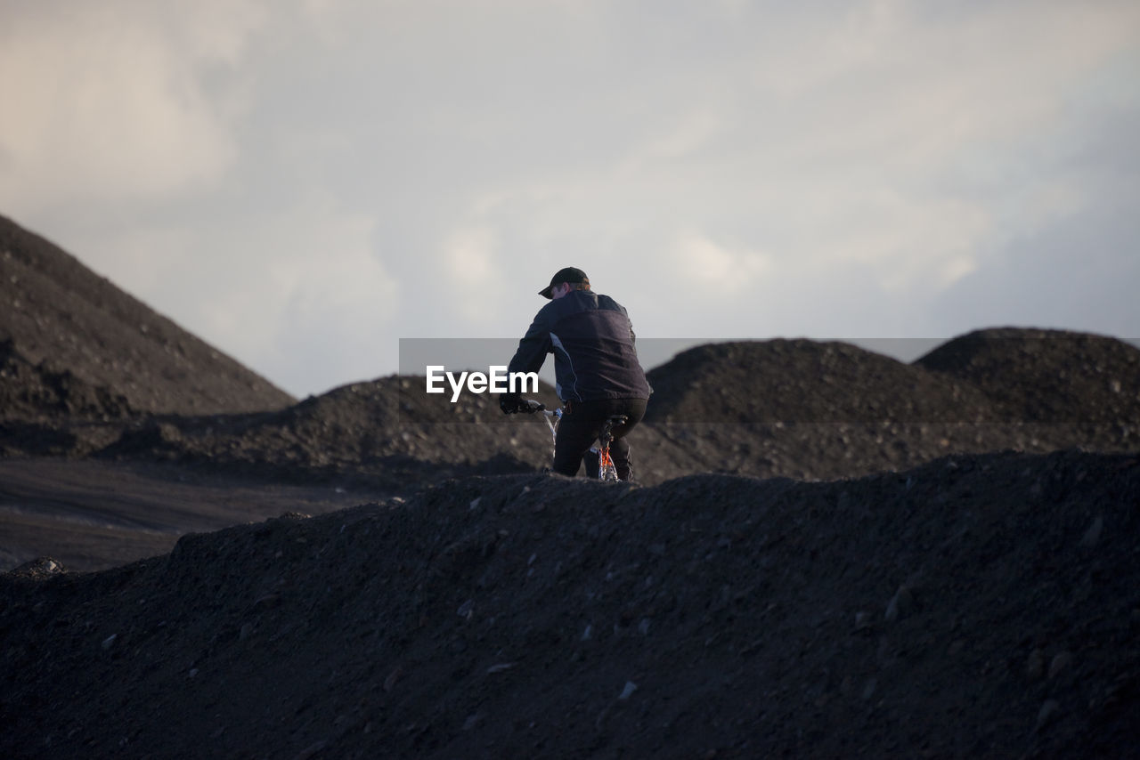 Rear view of man cycling amidst dirt heap