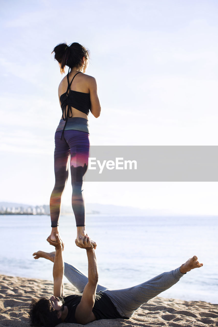 Couple performing yoga on shore against sky