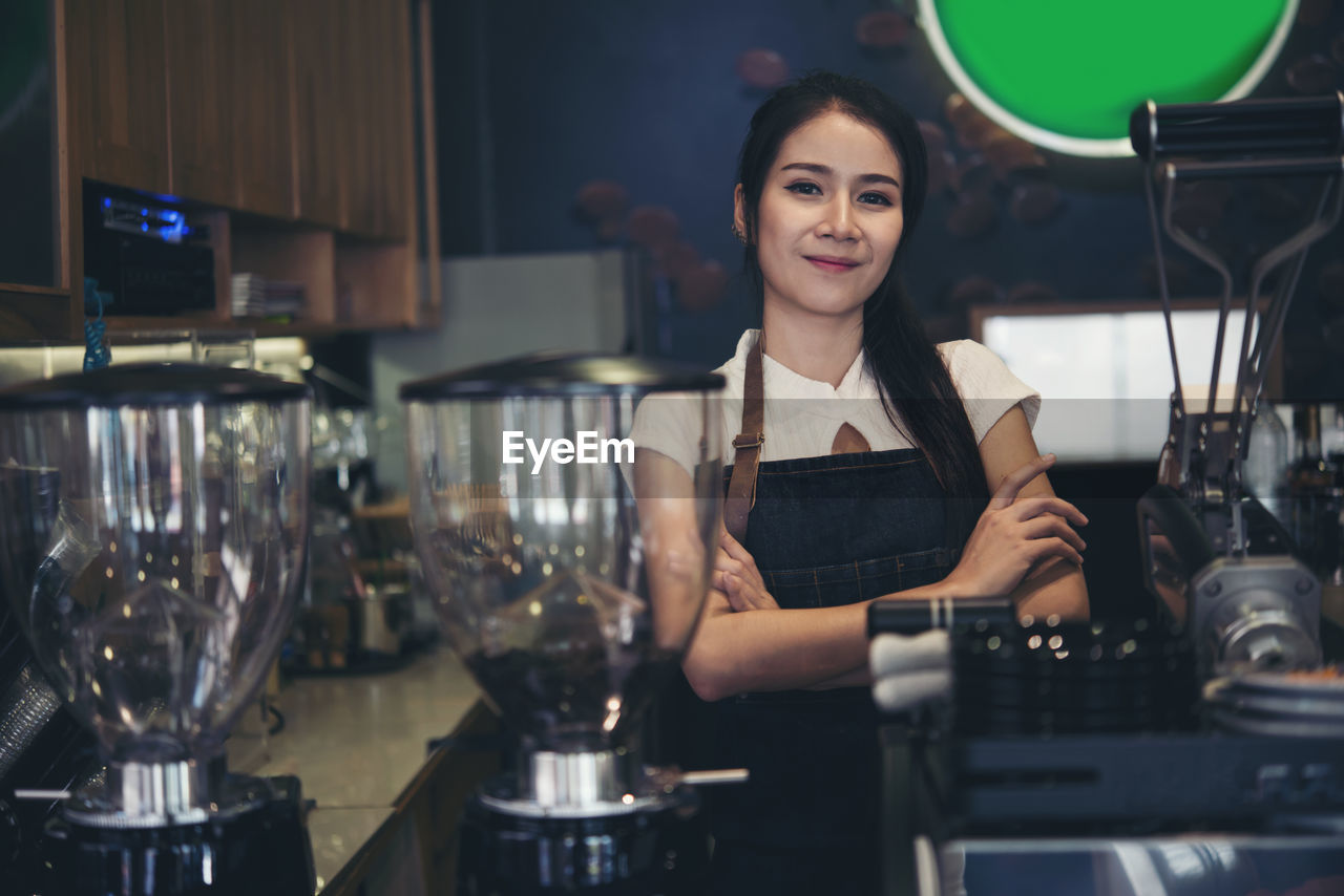 Portrait of smiling female barista with arms crossed standing at cafe