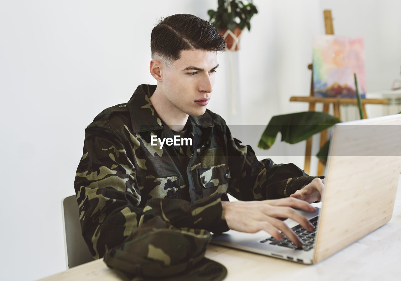 Young army man using laptop at home