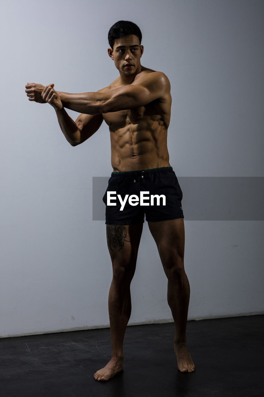 Shirtless muscular man exercising against wall