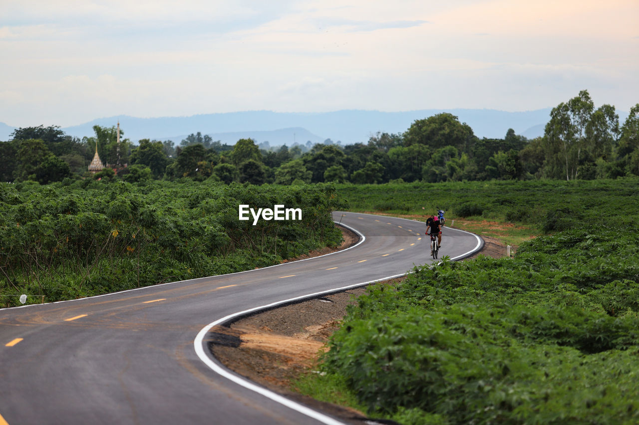 People riding bicycle on road against sky