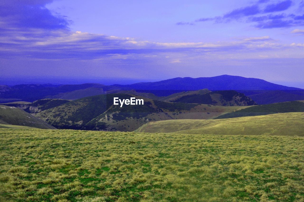 Grass covered mountain ranges against sky