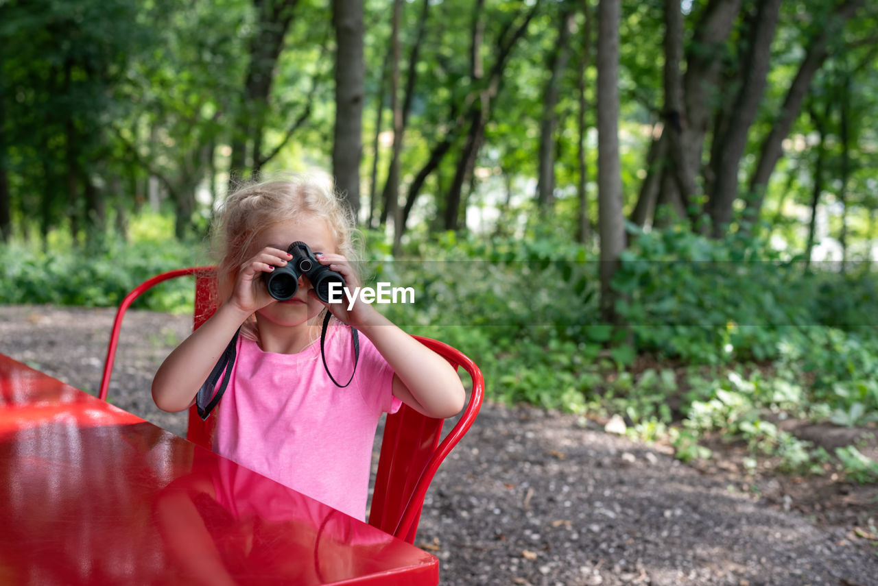 Close-up of girl looking through binoculars at table in forest