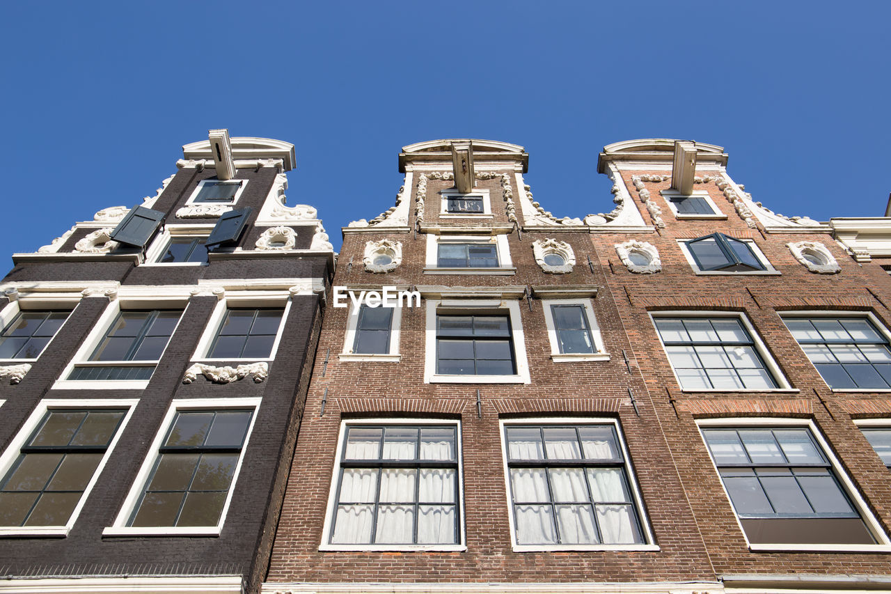 Low angle view of canal houses in amsterdam against clear blue sky