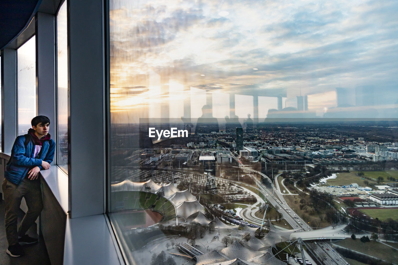 PORTRAIT OF MAN STANDING BY MODERN BUILDINGS AGAINST SKY