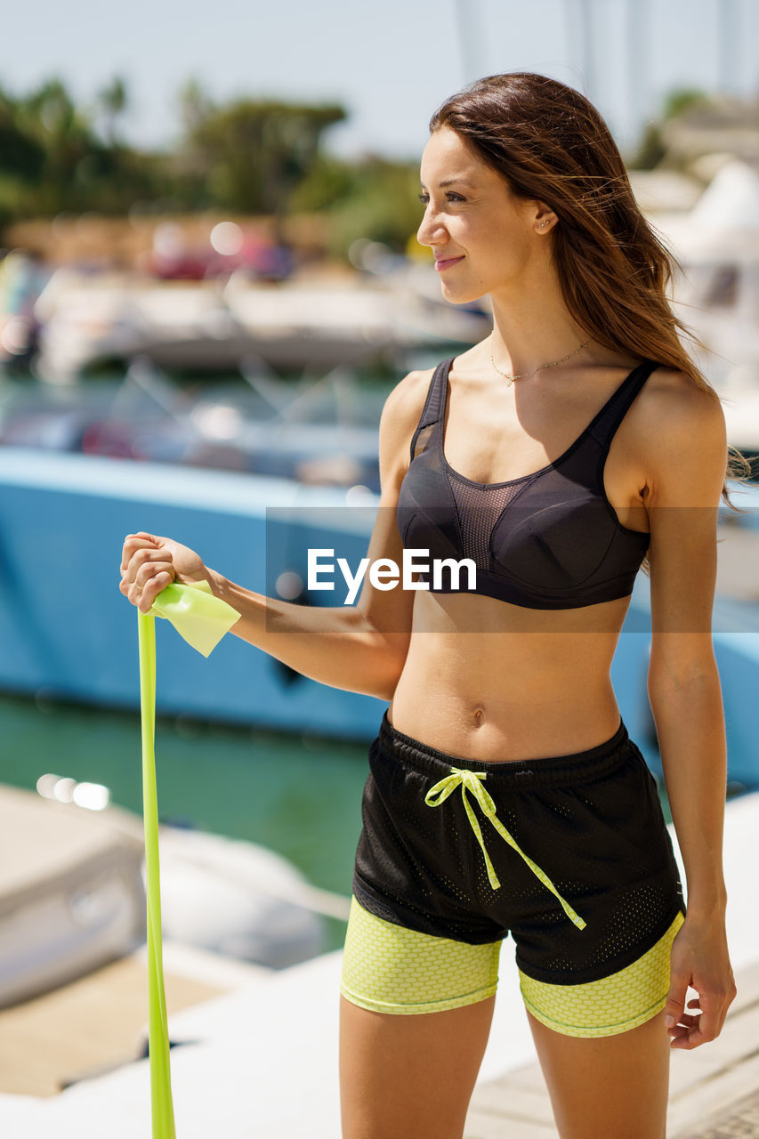 Smiling woman looking away while standing at harbor