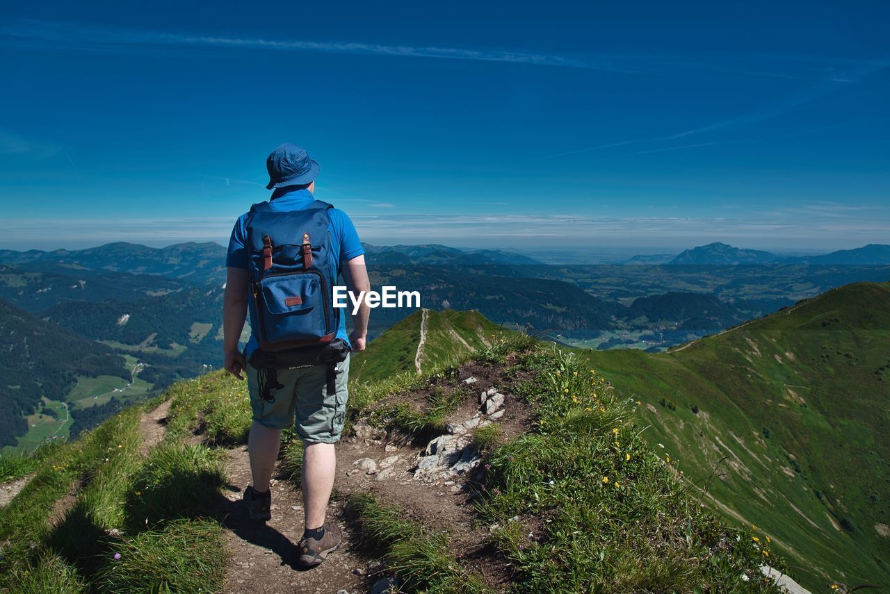 Rear view of hiker looking at mountains against blue sky