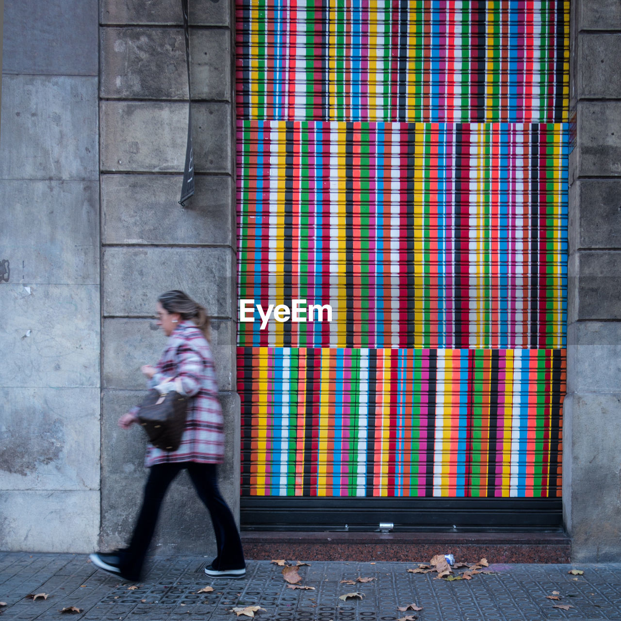 Side view of woman walking against colorful closed shutter