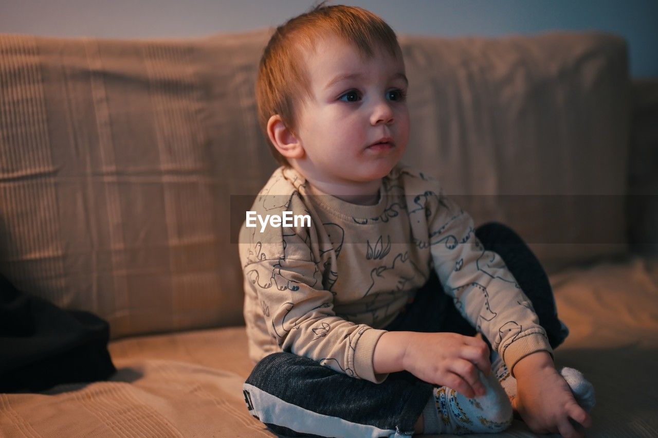 Portrait of cute little toddler sitting on a sofa and watching tv