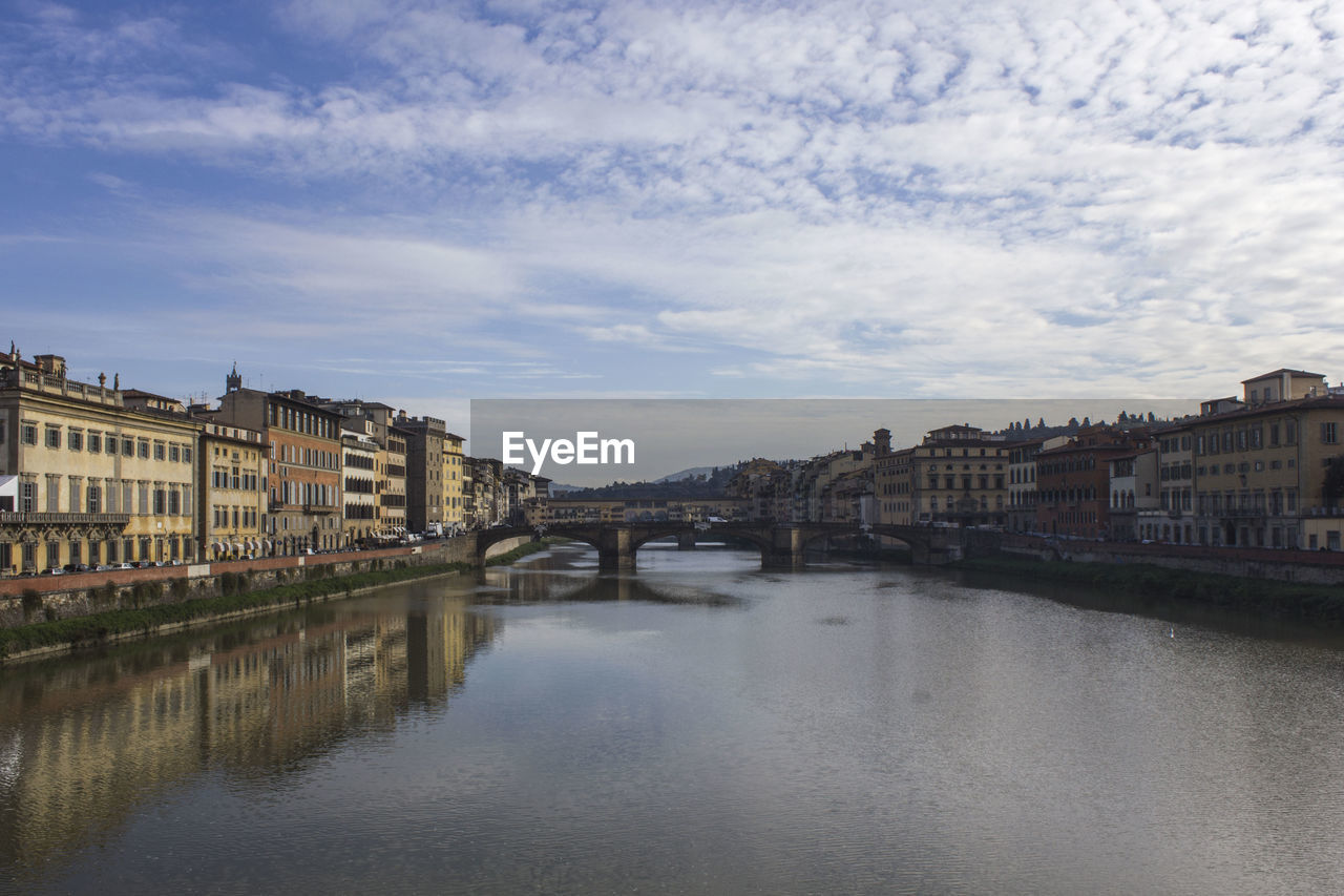 Bridge over river by buildings against sky