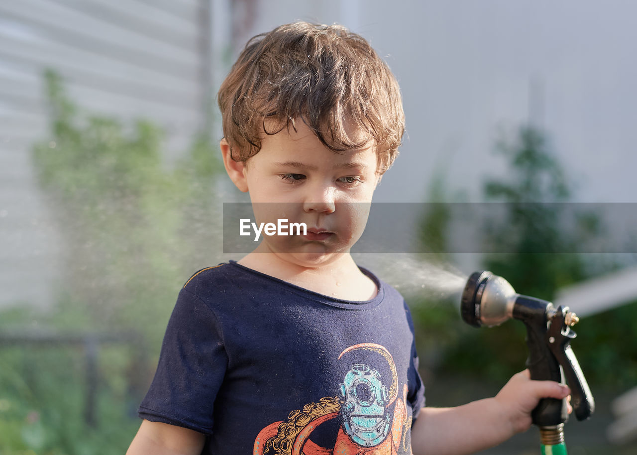 Little boy playing with a watering hose in the backyard