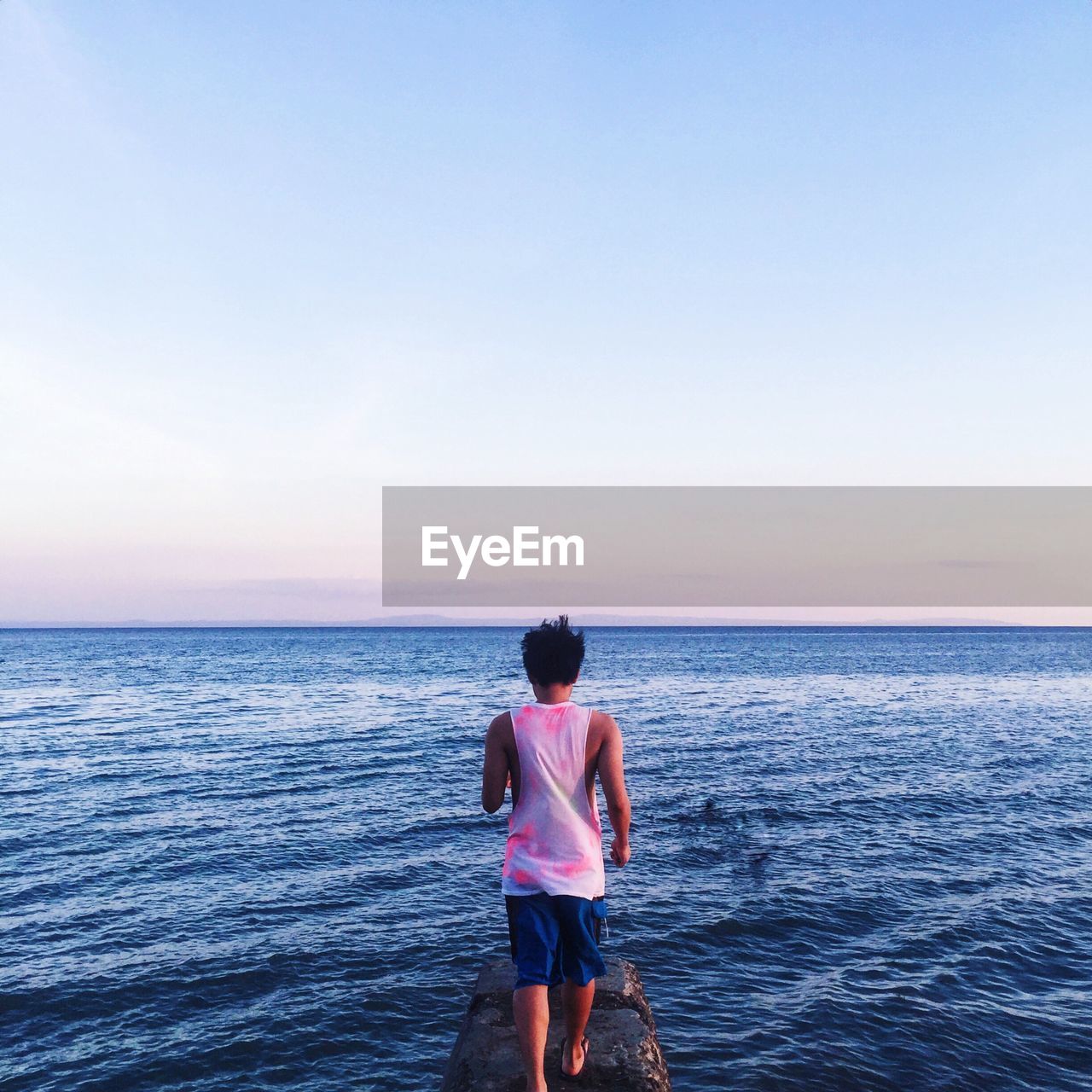 Rear view of man walking on jetty in sea against sky during sunset