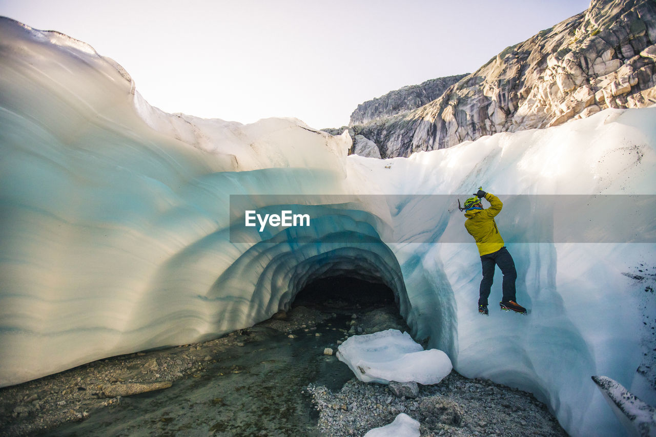 Man ice climbing next to glacial cave.