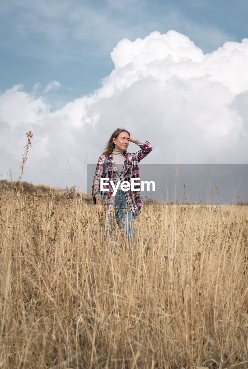 Woman looking away while standing on field against cloudy sky