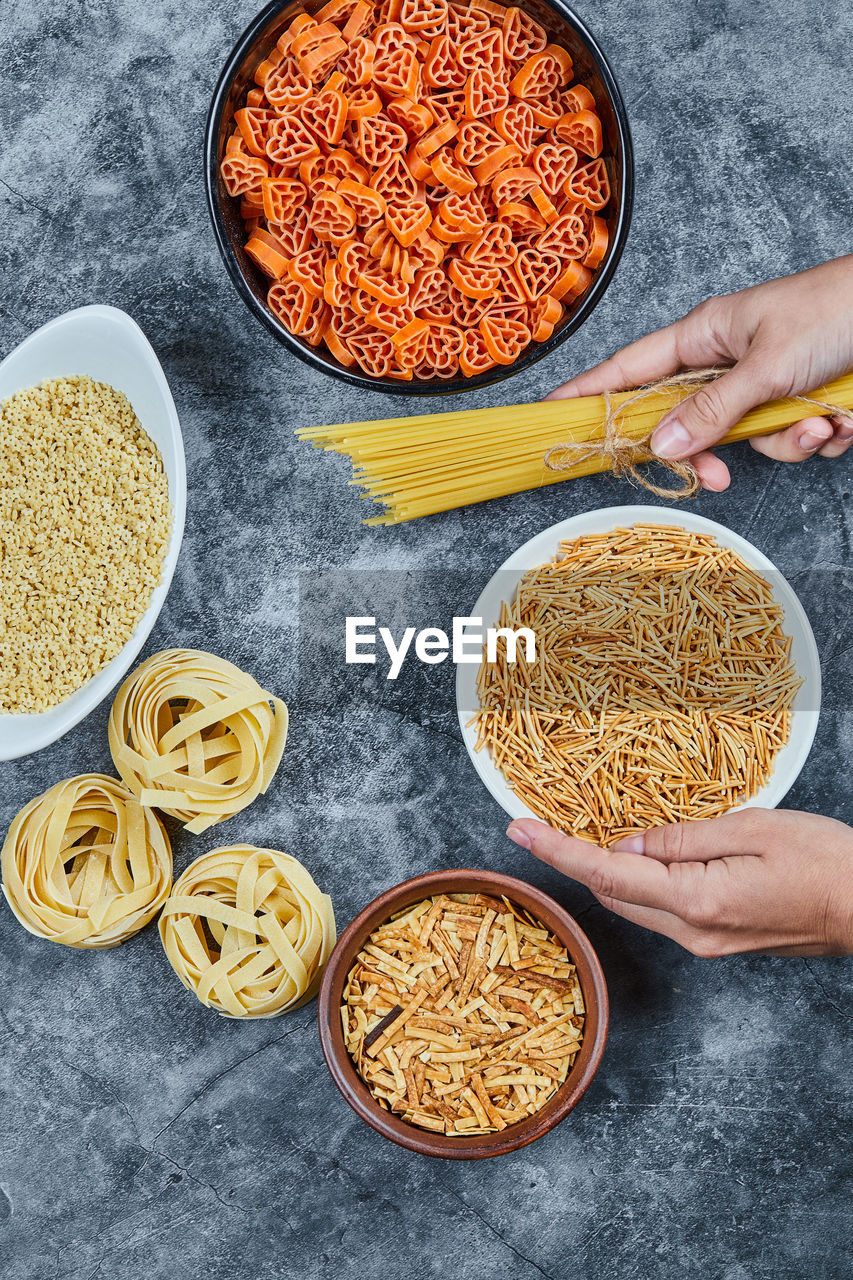 Hand holding a bowl of dry pasta with various types of raw pasta