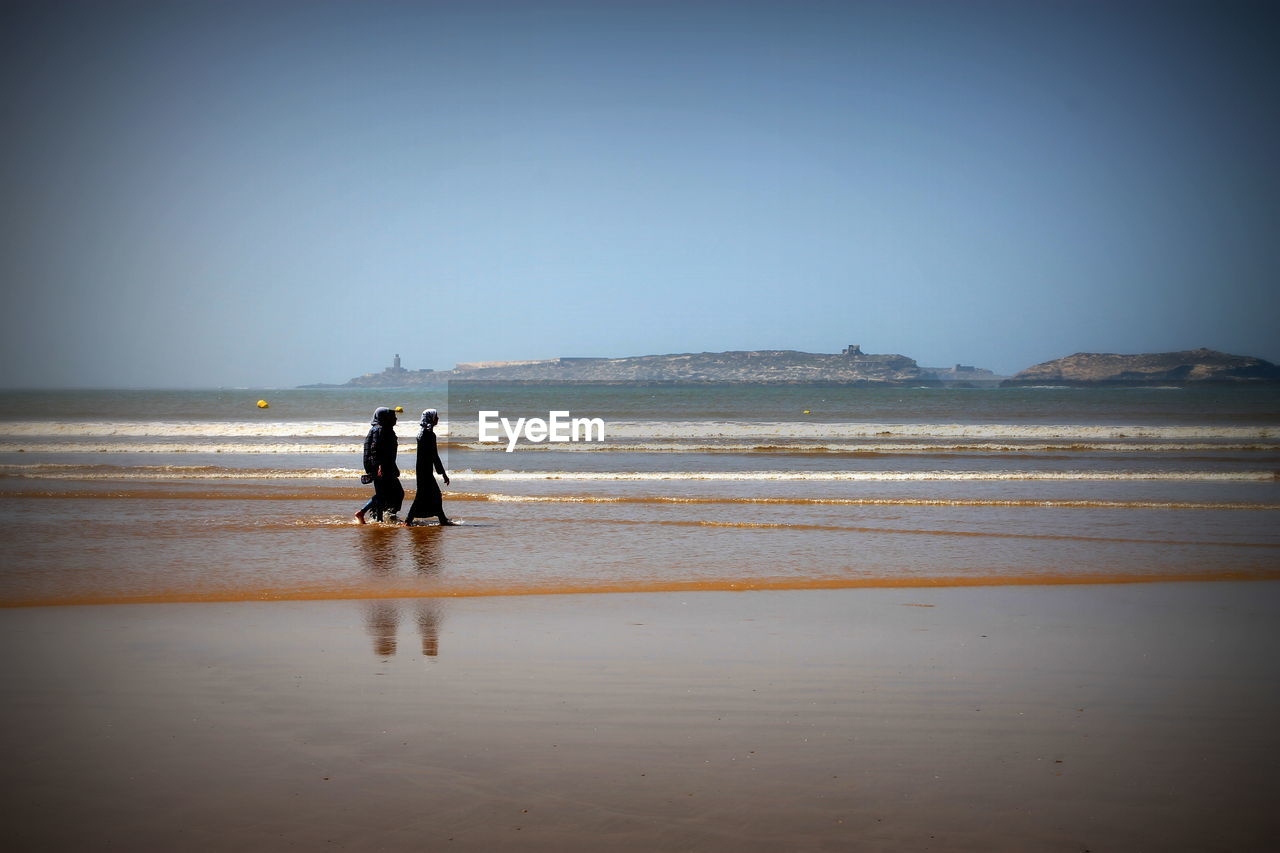 Side view of women walking at beach against clear sky