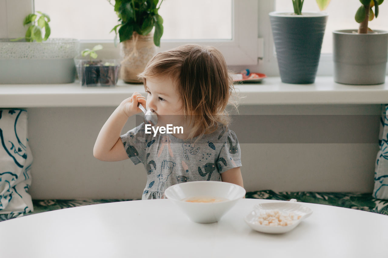 A little girl is sitting at the kitchen table eating soup. high quality photo