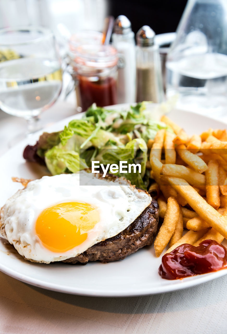 Close-up of fried egg with french fries and meat served on table