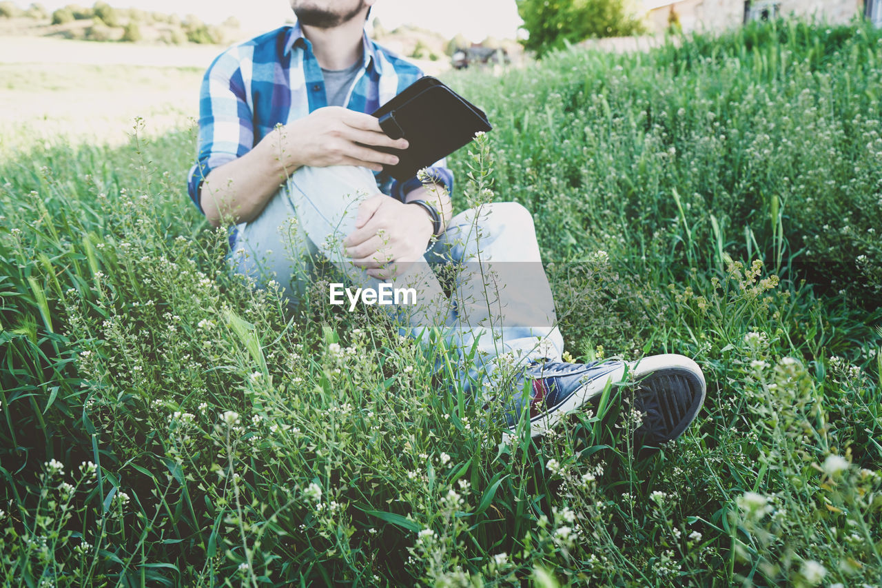 MAN USING PHONE WHILE SITTING ON GRASS