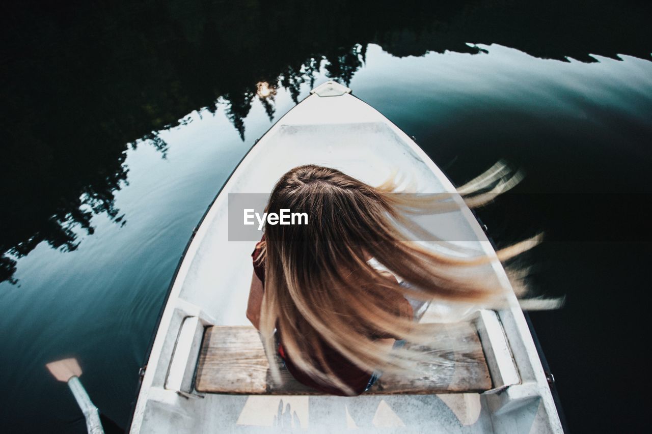 Rear view of woman tossing hair while sitting on boat in lake