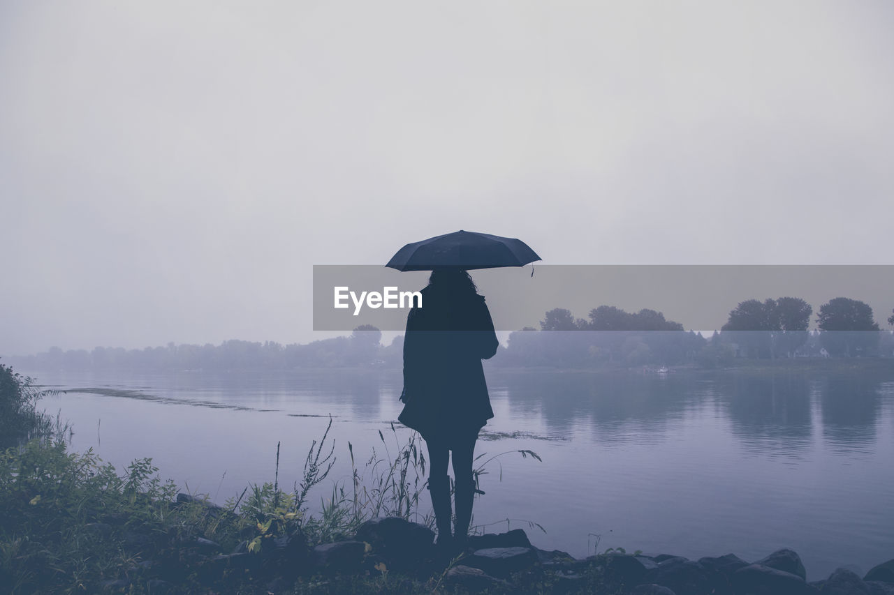 Silhouette woman standing by lake against sky