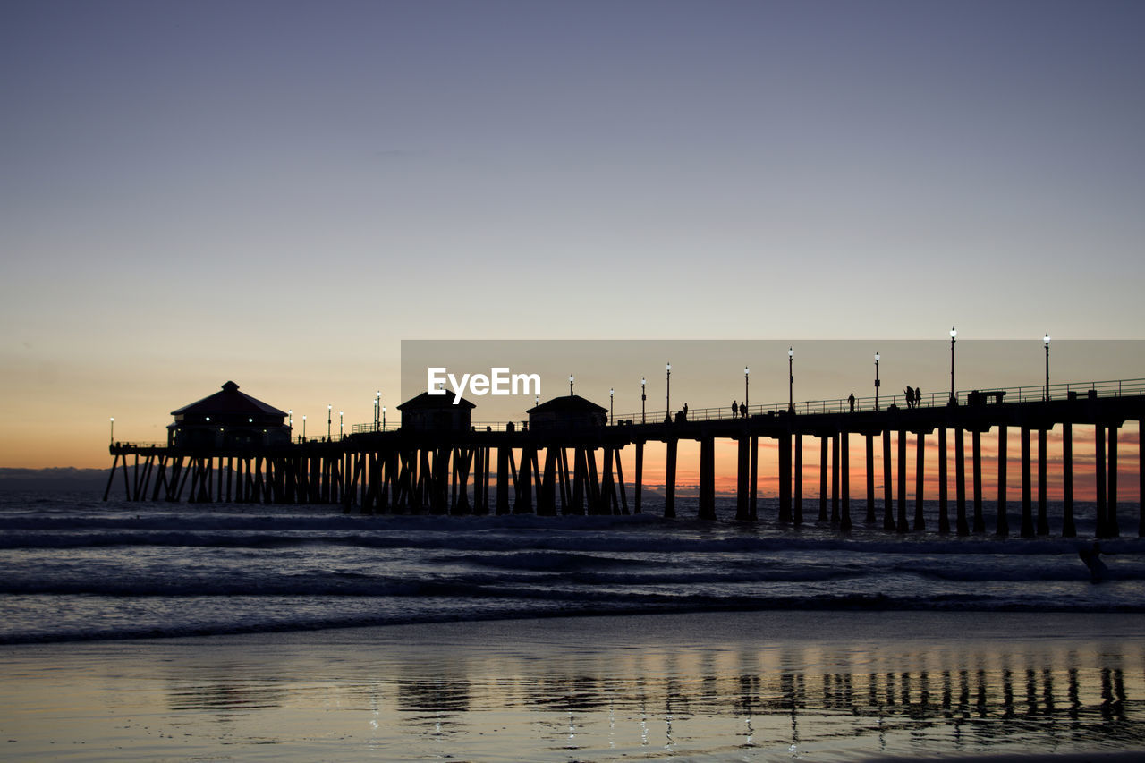 Silhouette pier on beach against clear sky during sunset