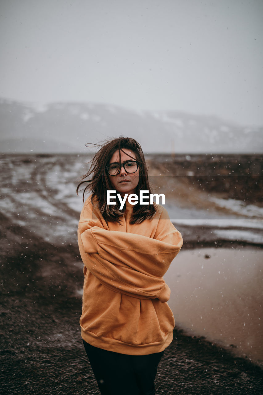 Young happy tourist in eyeglasses with piercing looking at camera between deserted ground in snow