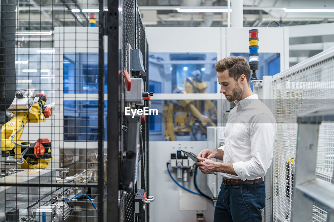 Businessman using tablet at a robot in a modern factory