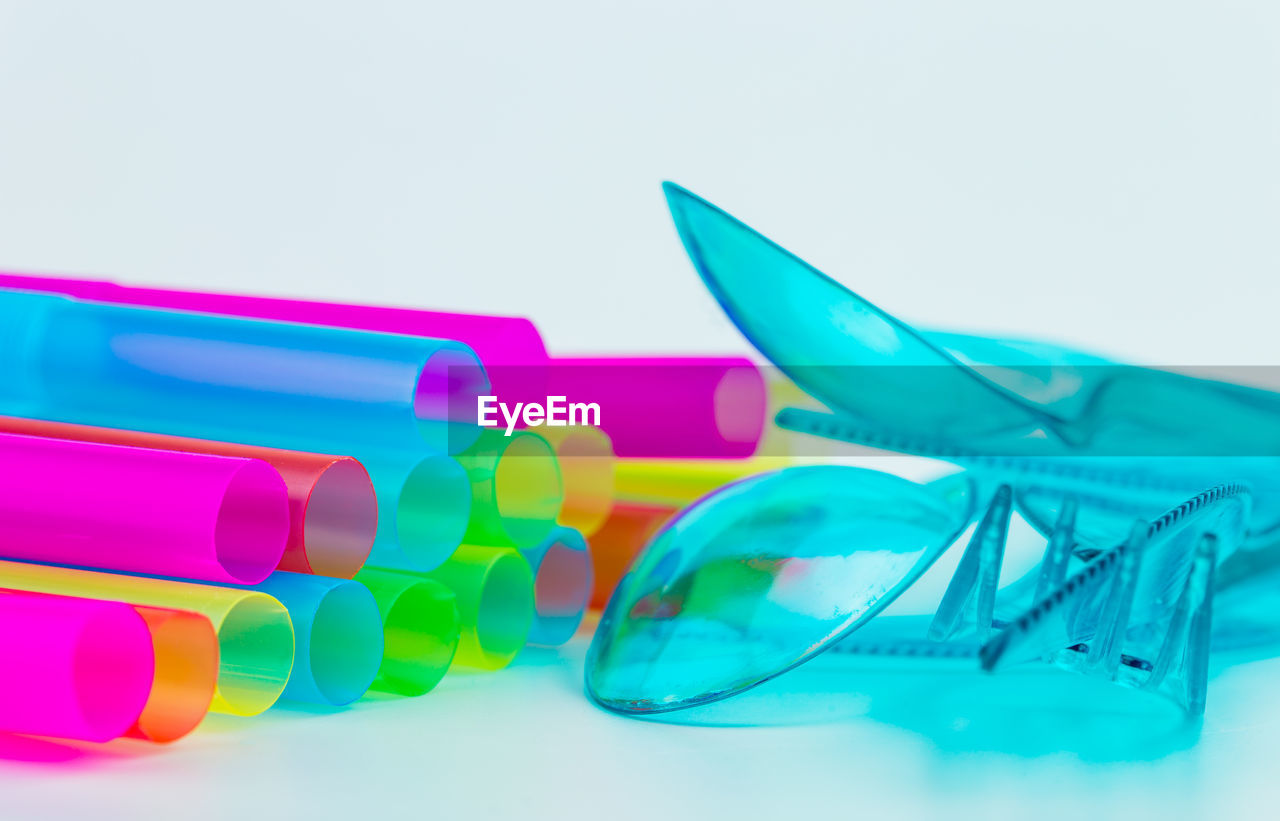 Close-up of plastic eating utensils and drinking straws over gray background