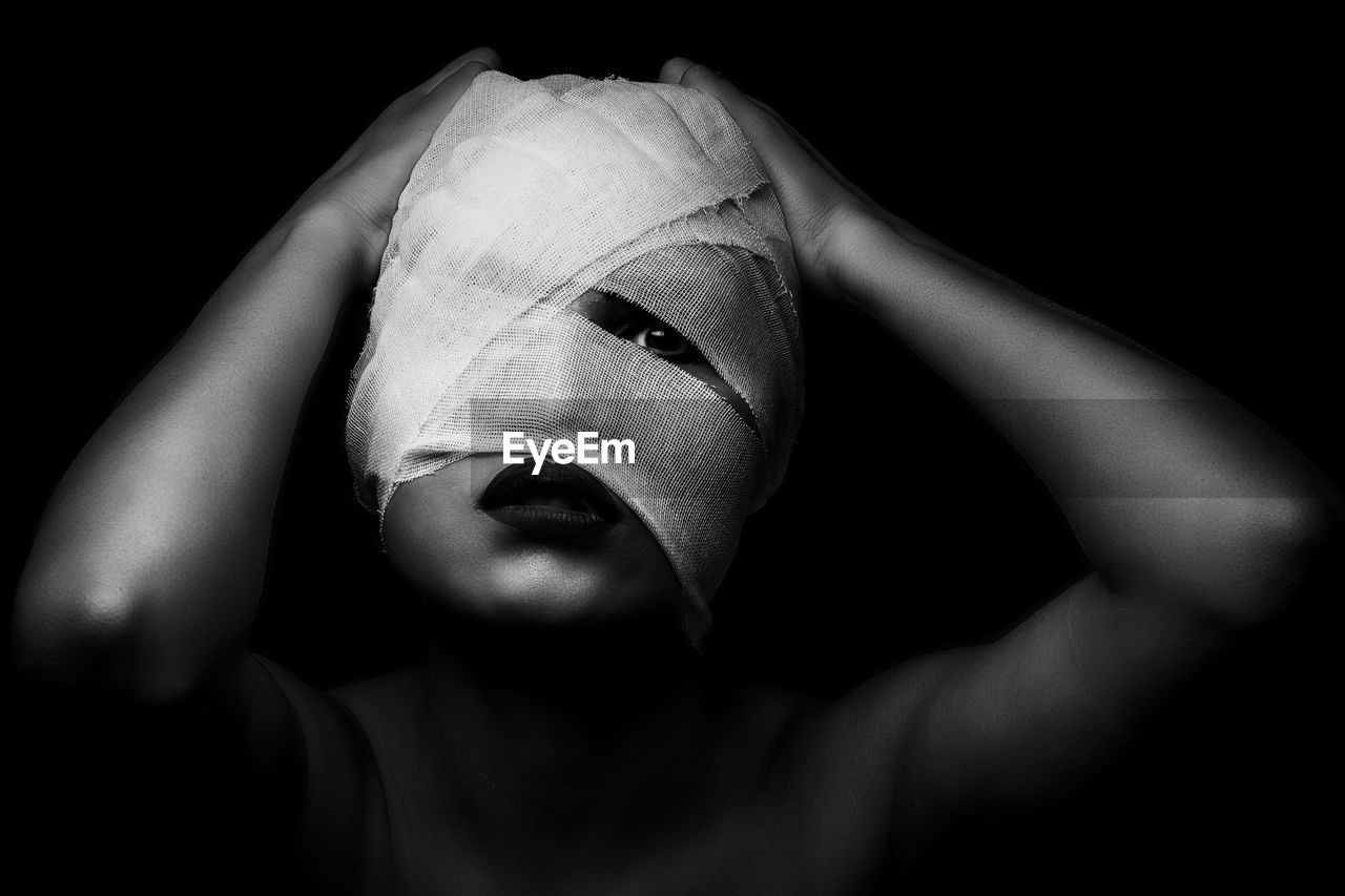 Close-up portrait of young woman face wrapped in bandage against black background