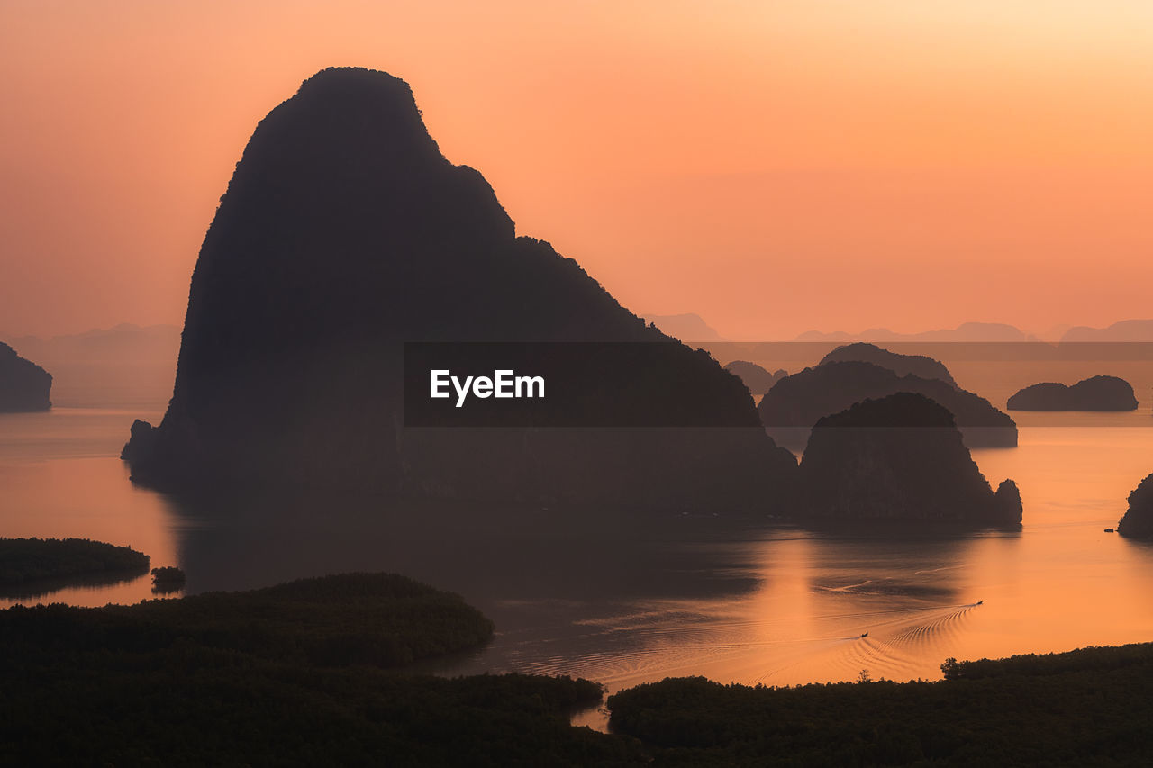 Silhouette rock formation in sea against sky during sunset