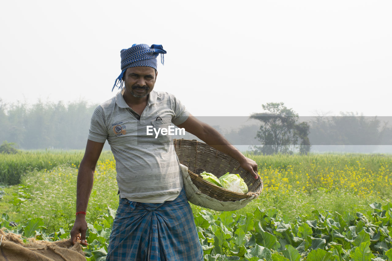 Full length of young farmer standing on field with vegetable basket