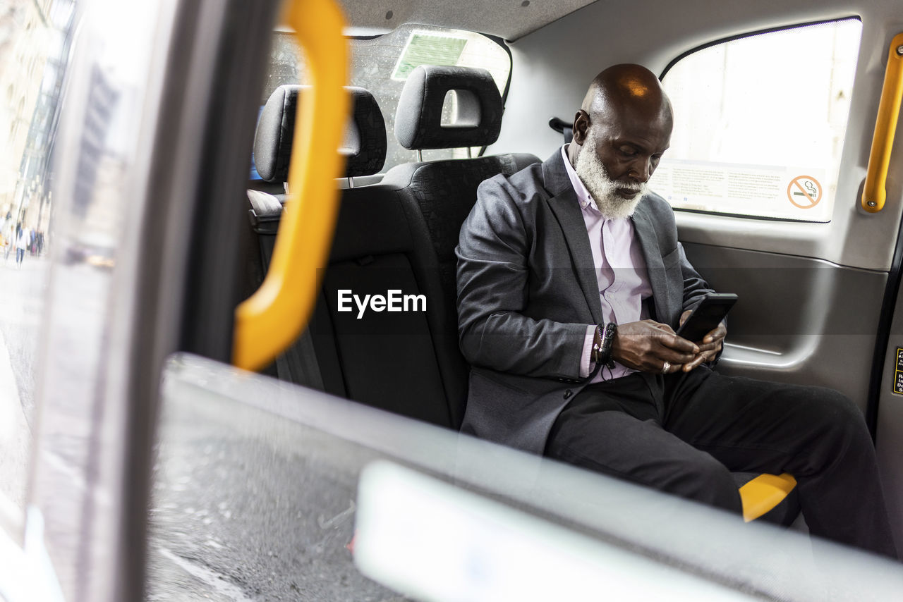 Senior businessman using mobile phone in taxi