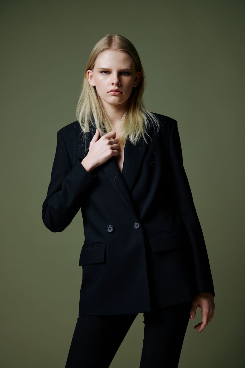 one person, studio shot, formal wear, adult, blond hair, portrait, women, indoors, young adult, business, clothing, outerwear, looking at camera, standing, hairstyle, long hair, tuxedo, coat, front view, colored background, three quarter length, female, photo shoot, person, collar, businesswoman, fashion, blazer, gray, serious, jacket, gray background, looking