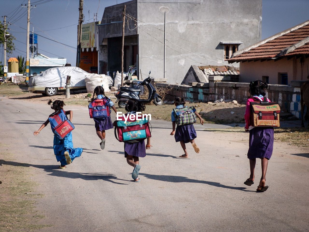 Rear view of schoolgirls running on street in town