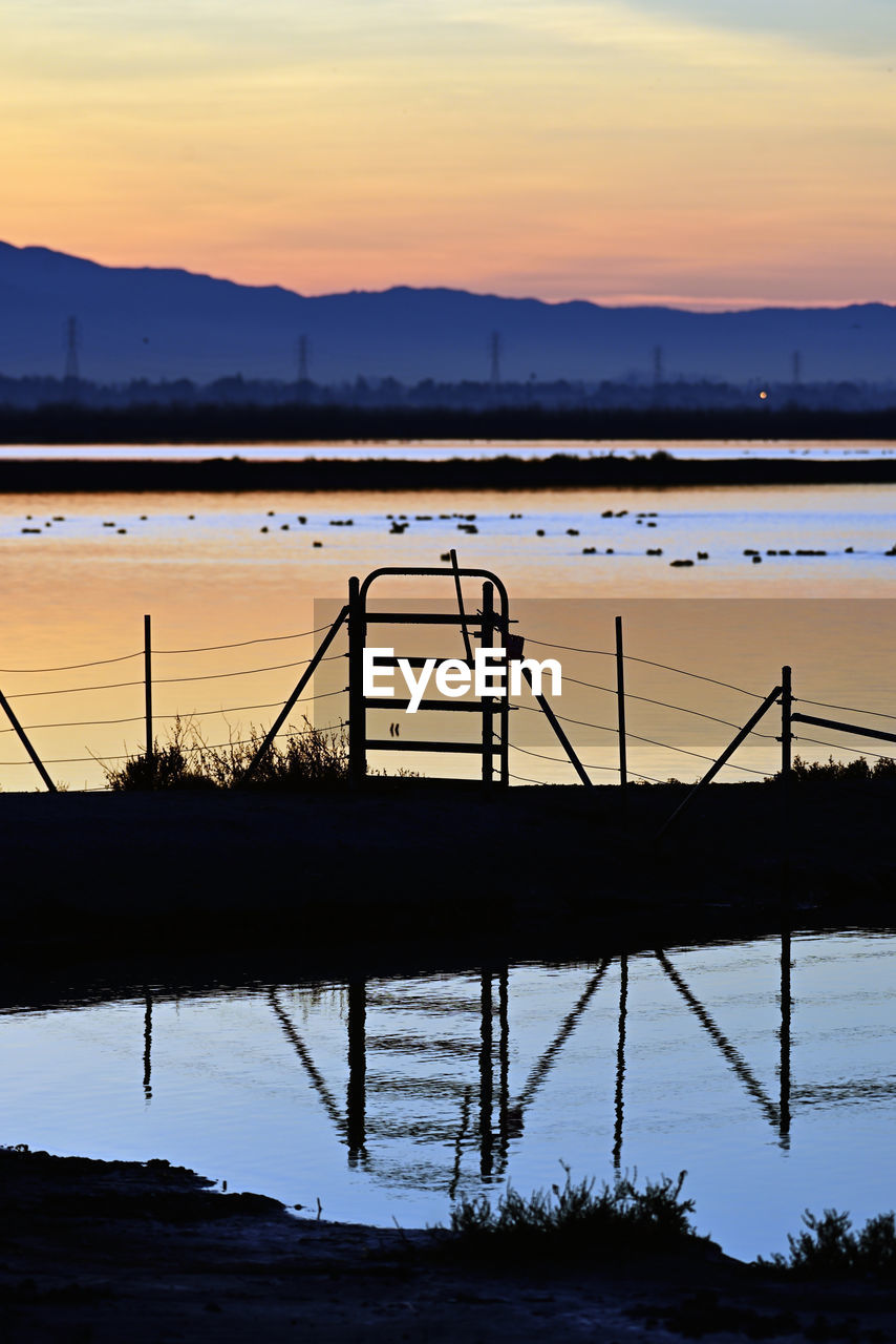 reflection, water, sunset, sky, dusk, sea, evening, nature, horizon, silhouette, architecture, beauty in nature, ocean, dock, cloud, scenics - nature, shore, tranquility, no people, mountain, built structure, pier, tranquil scene, outdoors, transportation, bay, coast, environment, land, beach, landscape