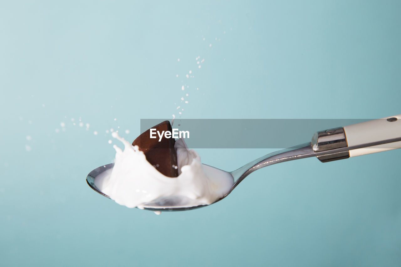 Close-up of chocolate splashing milk on spoon against blue background