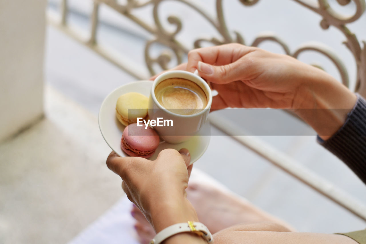 Cropped image of woman holding coffee cup with macaroons in saucer