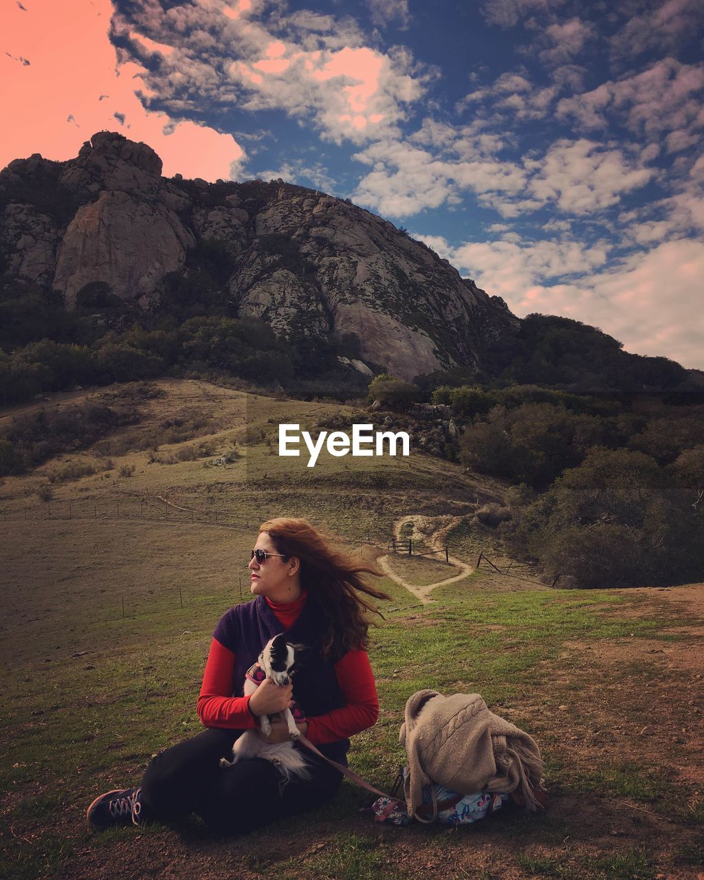 Young woman looking away sitting with dog on field