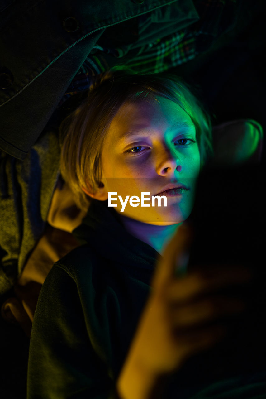 Portrait of tween looking at tablet with colorful light cast on face