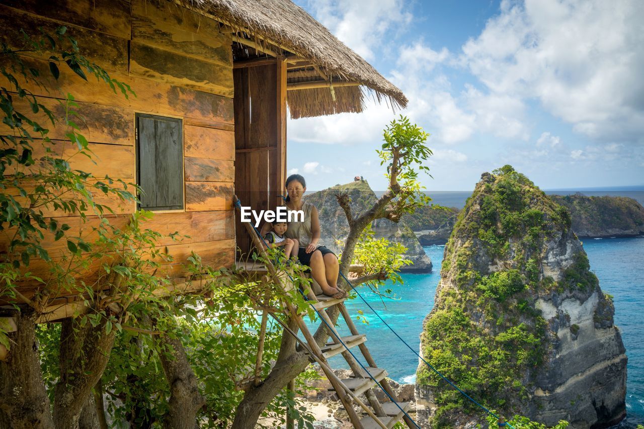 Portrait of mother with son sitting on steps at hut against sea