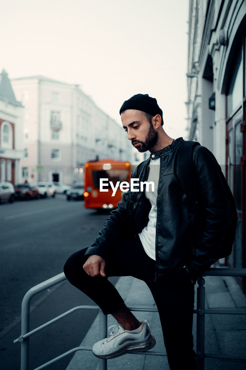 Young man looking away while sitting on street in city