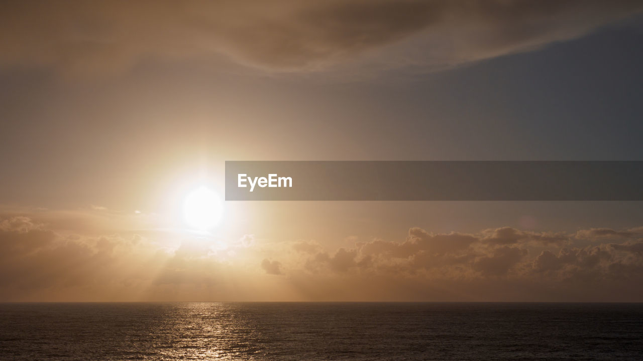 SCENIC VIEW OF SEA AGAINST BRIGHT SUN DURING SUNSET