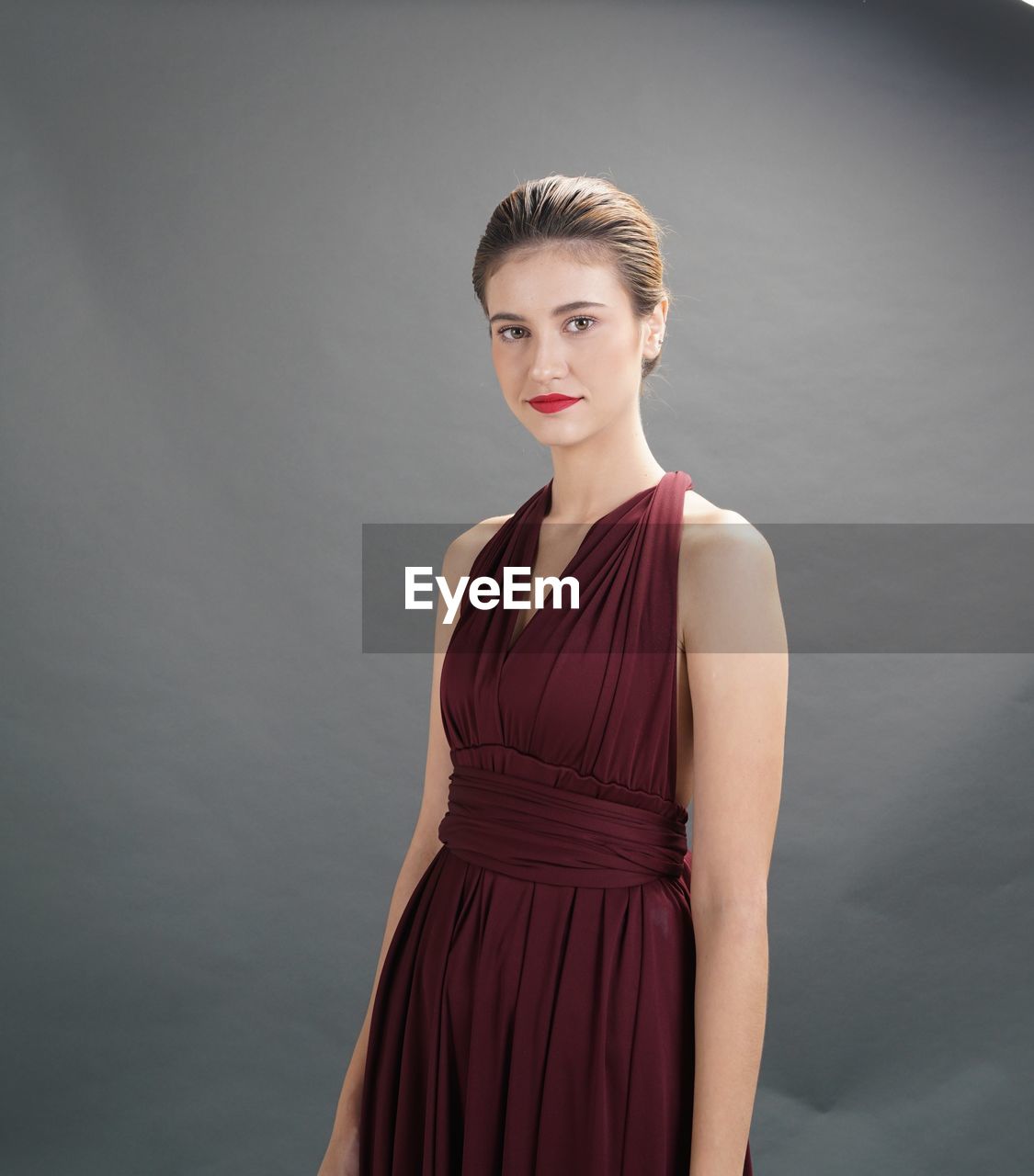 Portrait of young woman standing against gray background