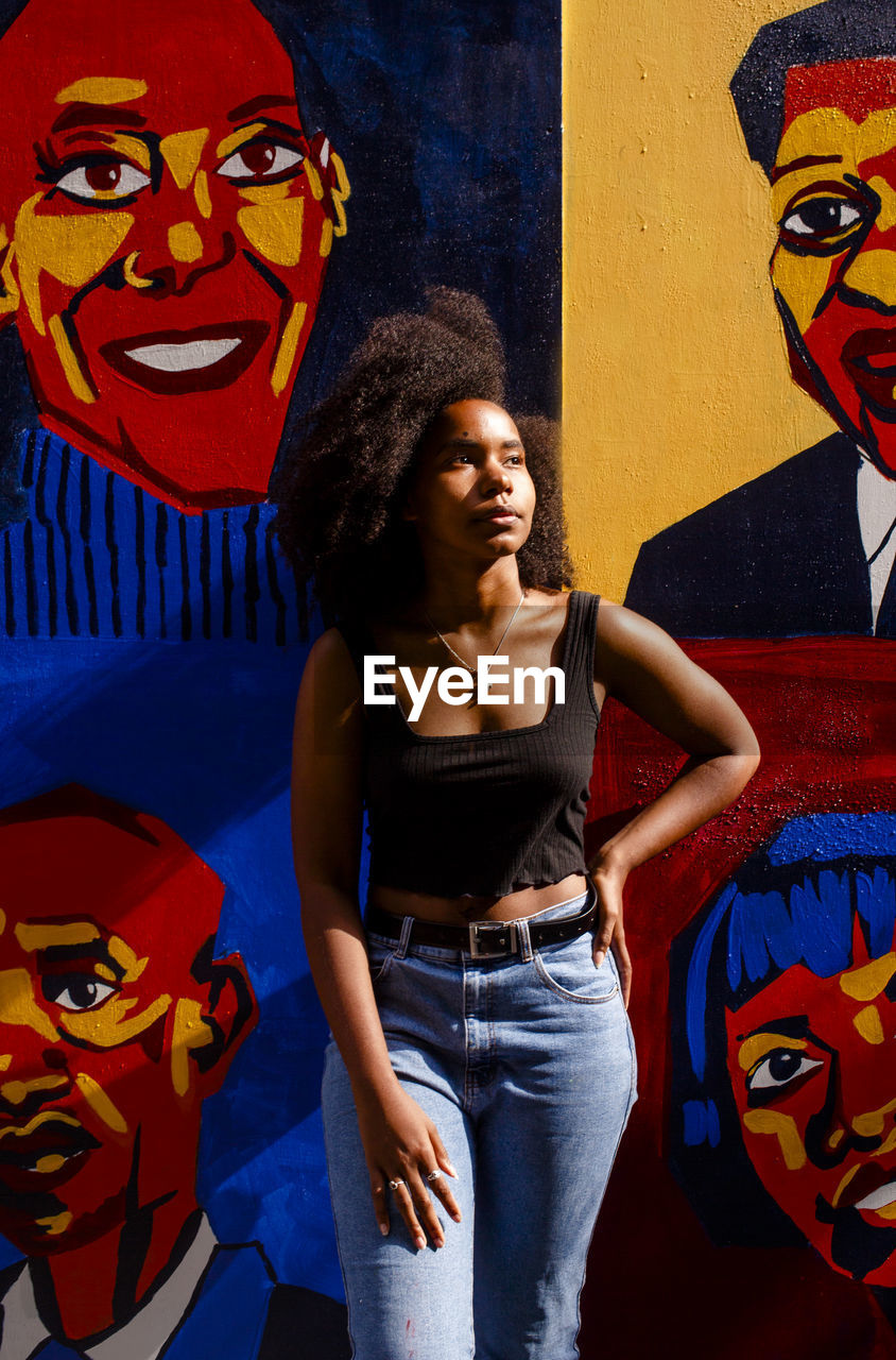 A beautiful young artist in golden light leans back against her mural