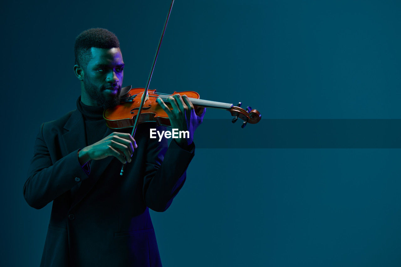 midsection of man playing violin against clear blue background