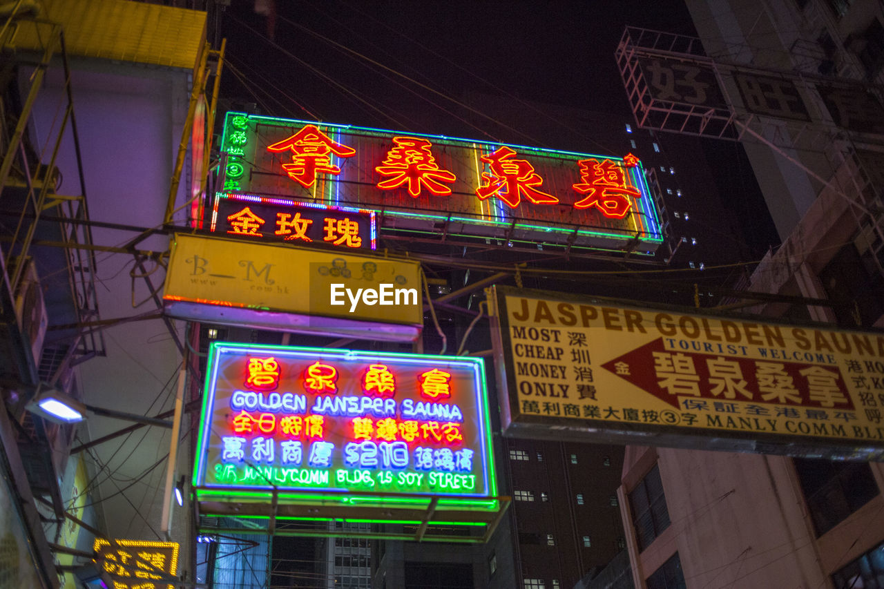 LOW ANGLE VIEW OF ILLUMINATED INFORMATION SIGN AGAINST BUILDING AT NIGHT